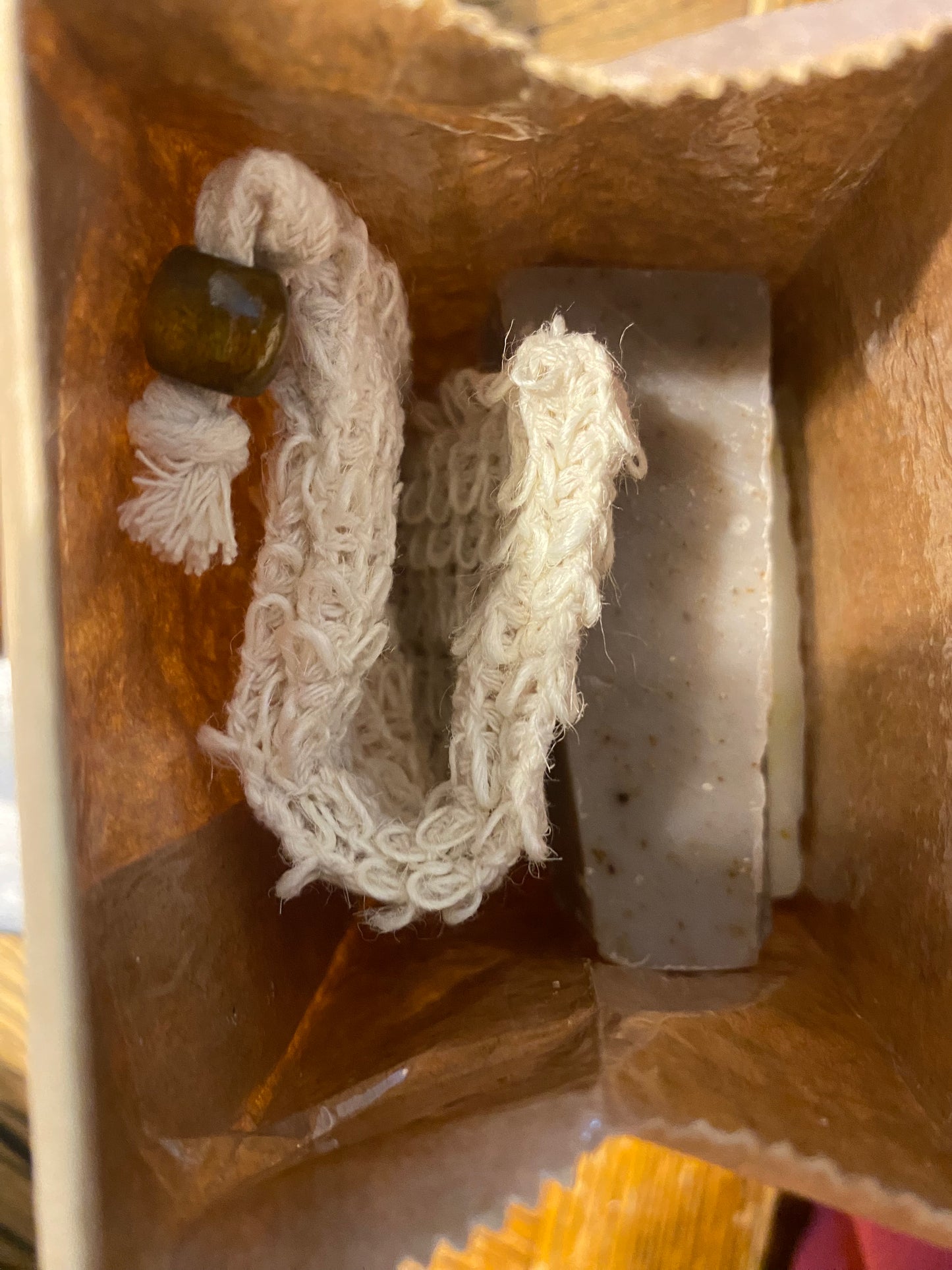 A close-up view of handmade soap odds and ends with a mesh soap saver bag packaged inside a brown paper bag.