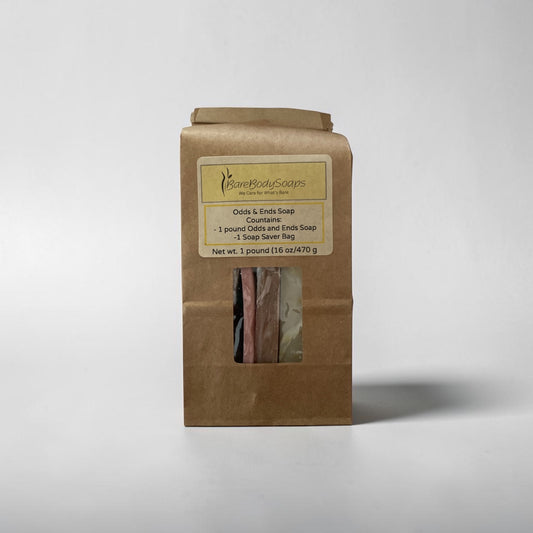 A brown kraft paper bag package of Some Bodies Soaps Odds & Ends Soap Countenance, featuring a clear window showing several bars of soap inside, set against a plain light gray background.